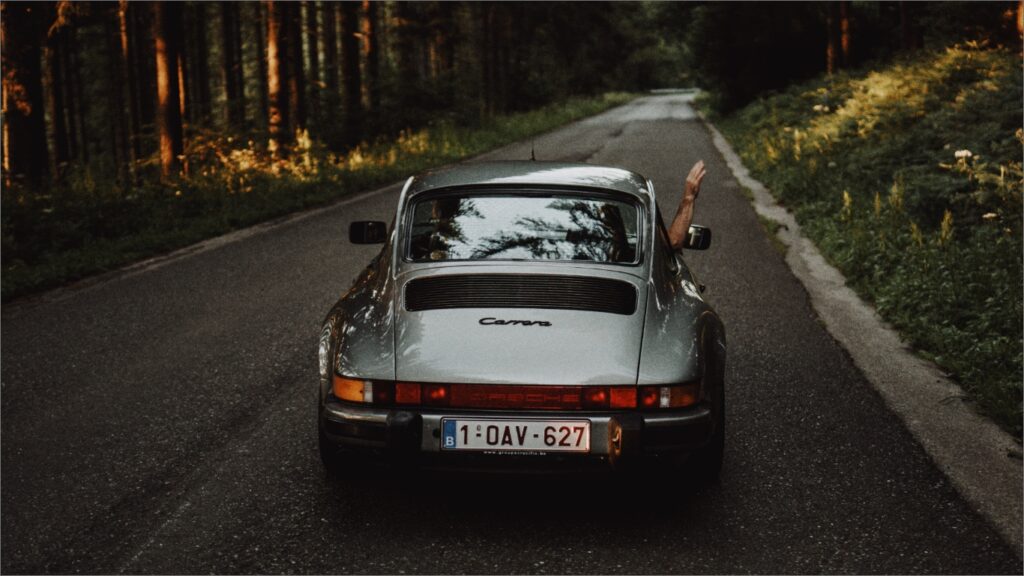 森の道を走るクラシックカーと手を出すドライバー